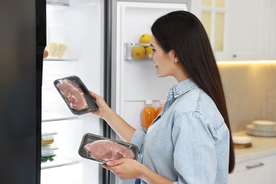Young woman taking packs of meat out of refrigerator in kitchen