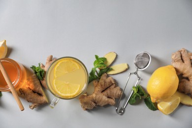 Photo of Glass of aromatic ginger tea and ingredients on light grey background, flat lay. Space for text