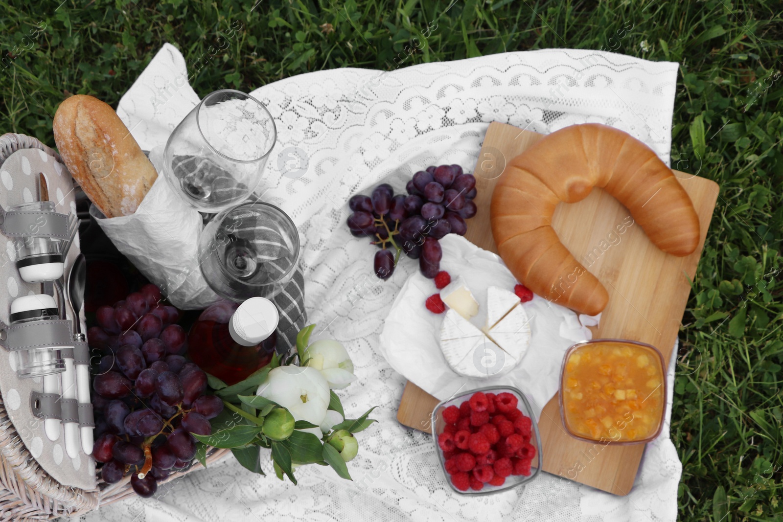 Photo of Picnic blanket with tasty food, flowers, basket and cider on green grass outdoors, flat lay