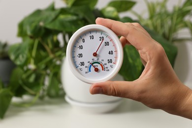 Photo of Woman holding round hygrometer with thermometer on blurred background, closeup