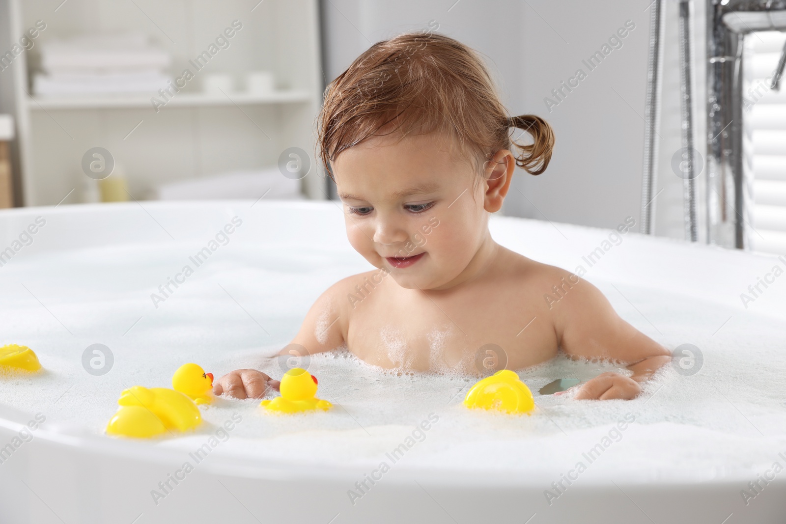 Photo of Cute little girl with rubber ducks in foamy bath at home