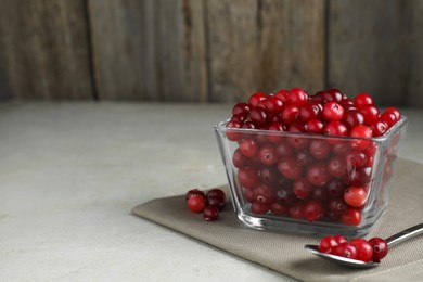 Photo of Cranberries in bowl and spoon on light grey table, closeup. Space for text