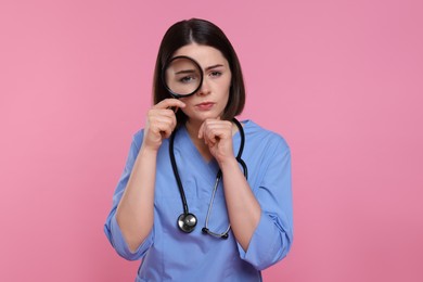 Photo of Doctor with stethoscope looking through magnifier on pink background
