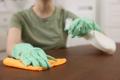 Photo of Woman with spray bottle and microfiber cloth cleaning wooden table in room, closeup