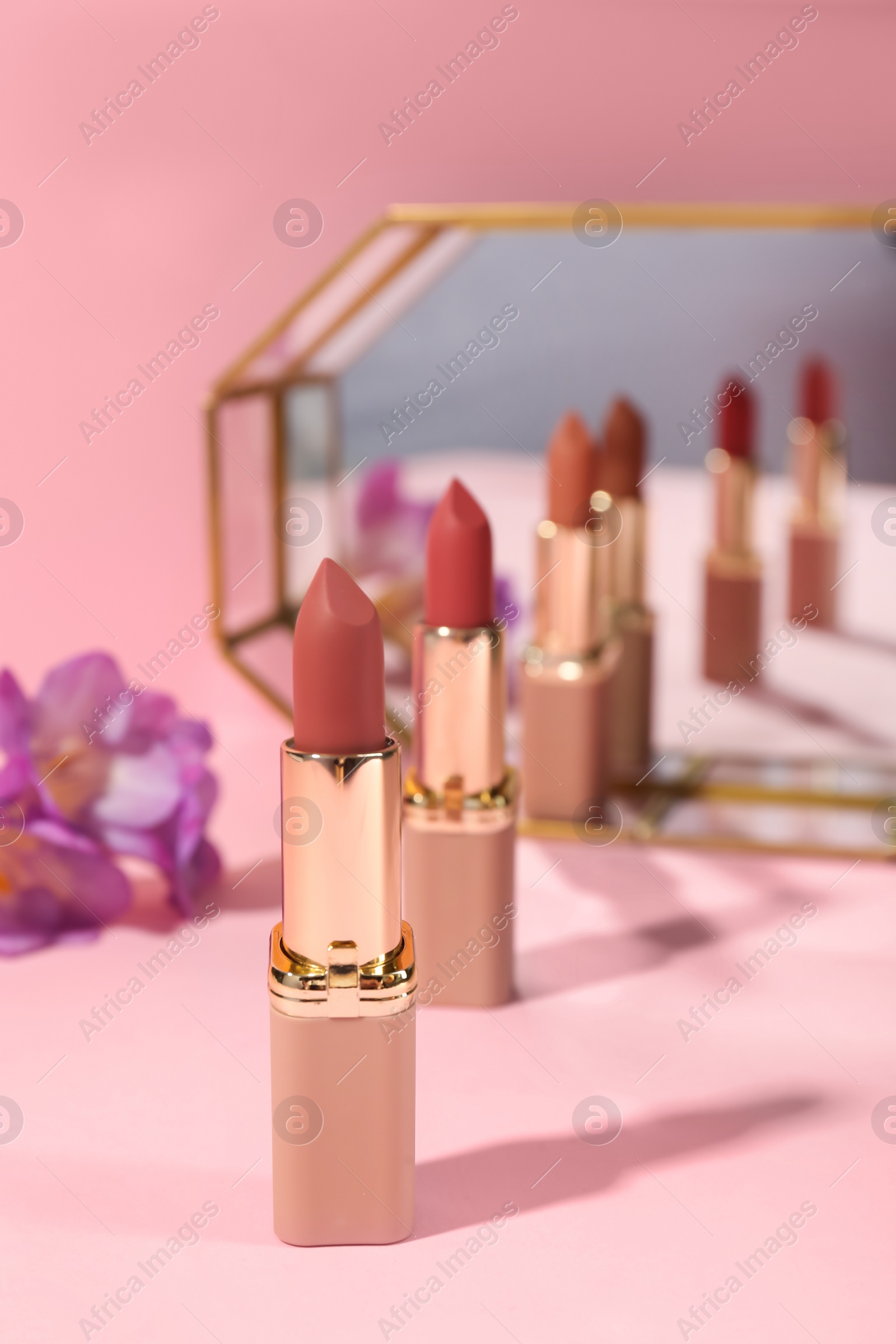 Photo of Different lipsticks and flower near mirror on pink background