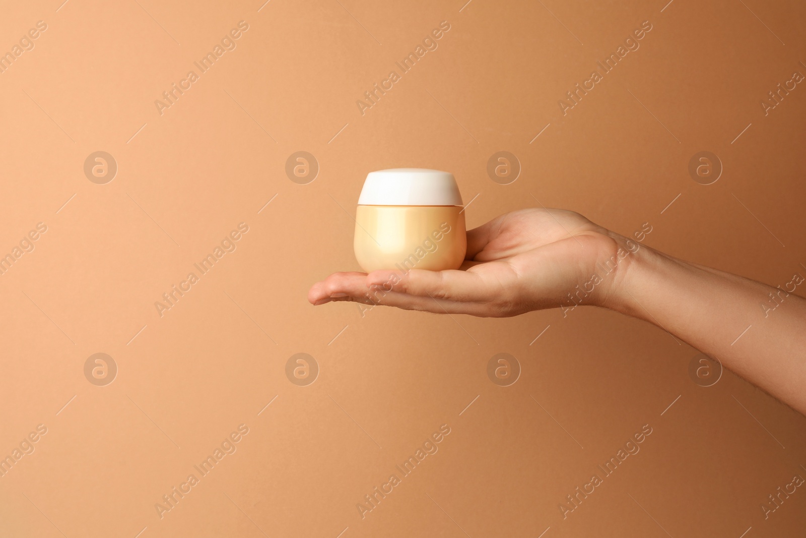 Photo of Woman holding jar of face cream on beige background, closeup. Space for text