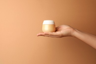 Photo of Woman holding jar of face cream on beige background, closeup. Space for text