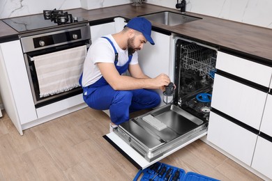 Photo of Repairman holding drain filter near dishwasher in kitchen