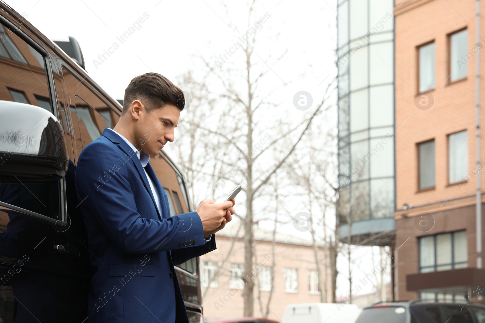 Photo of Handsome man with smartphone near modern car outdoors