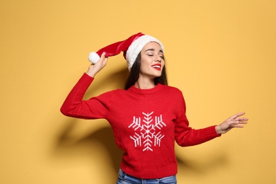 Photo of Young woman in Christmas sweater and hat on color background