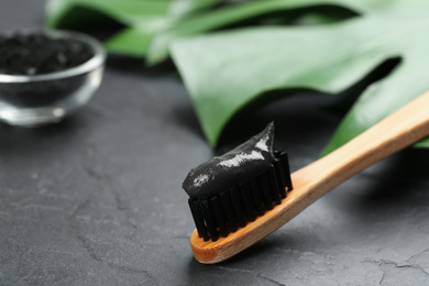Photo of Bamboo toothbrush with charcoal paste on black stone table, closeup. Space for text