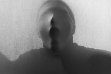 Photo of Silhouette of creepy ghost behind grey cloth. Black and white effect