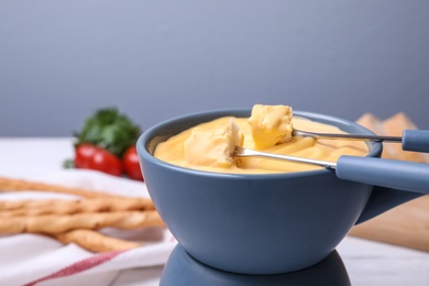 Pot with delicious cheese fondue and bread pieces on table