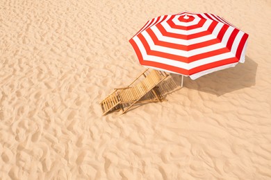 Image of Striped beach umbrella near wooden sunbed on sandy coast