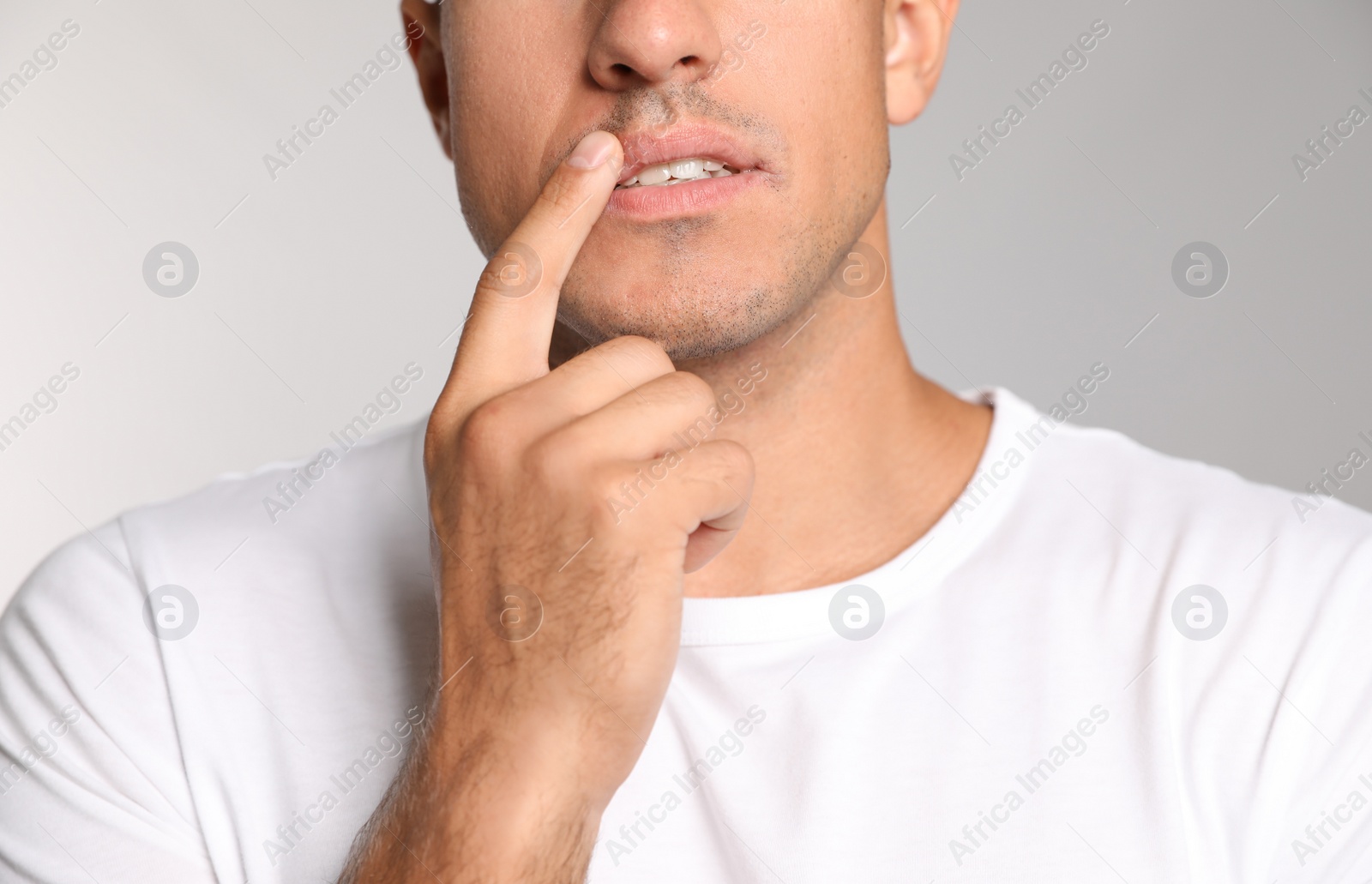 Photo of Man with herpes touching lips against light grey background, closeup