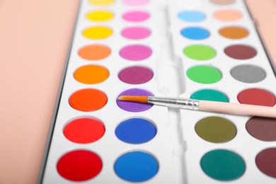 Photo of Watercolor palette with brush on beige background, closeup