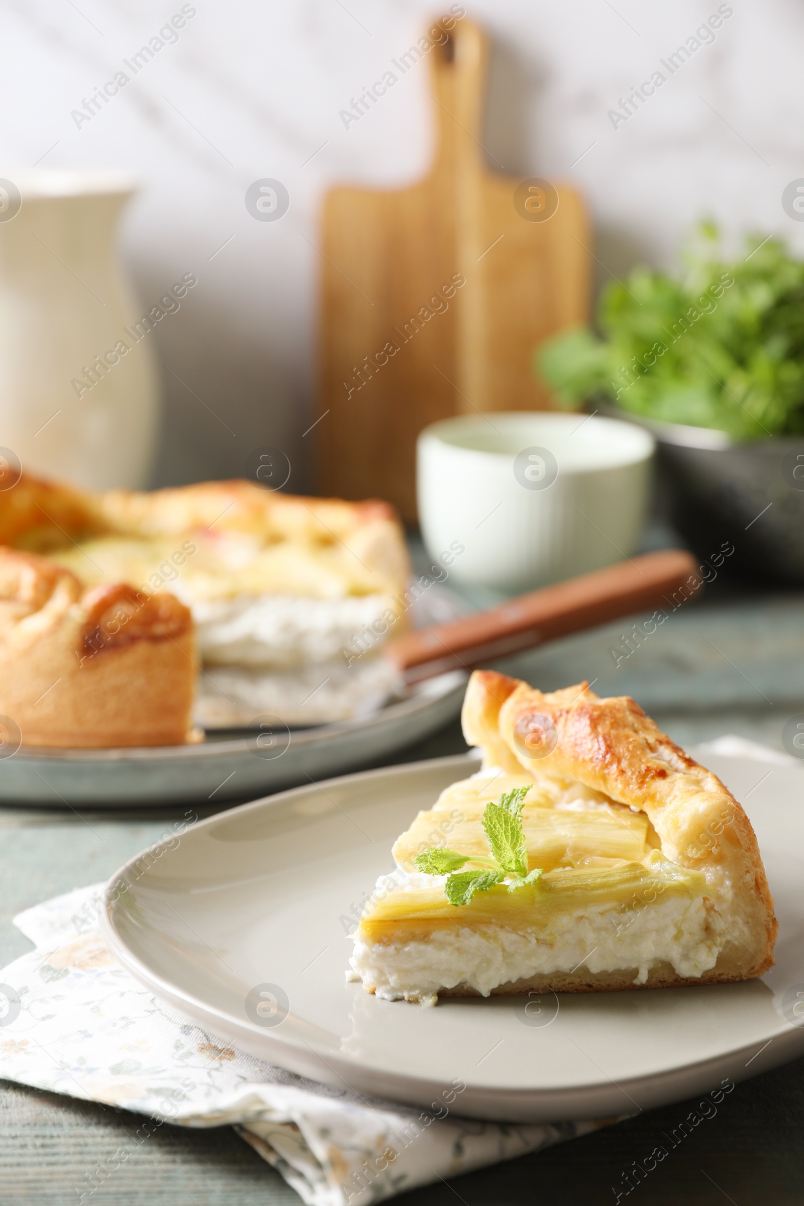 Photo of Piece of freshly baked rhubarb pie with cream cheese and mint leaves on grey wooden table