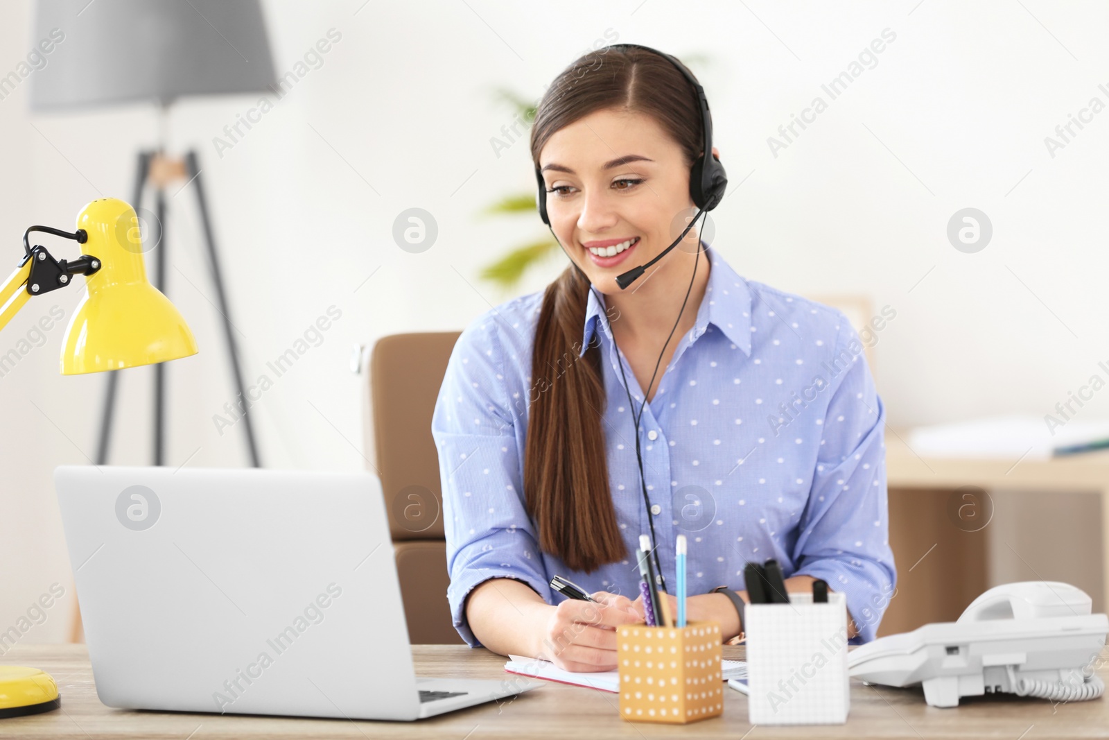 Photo of Young woman talking on phone through headset at workplace