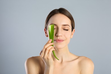 Photo of Young woman with aloe leaf on light grey background