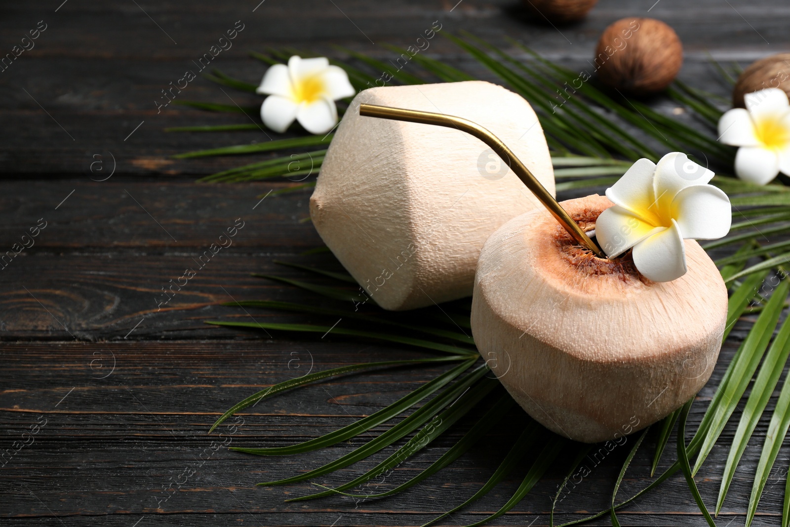 Photo of Fresh coconut with drinking straw and flower on black wooden table. Space for text