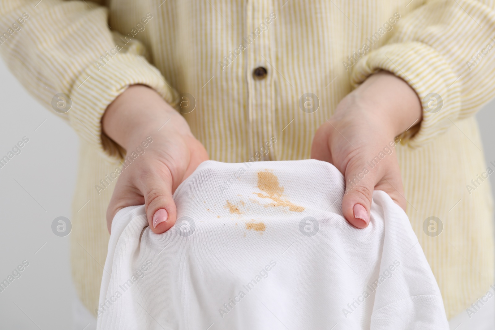 Photo of Woman holding shirt with stain against light background, closeup