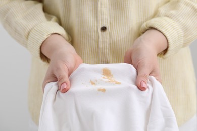 Woman holding shirt with stain against light background, closeup