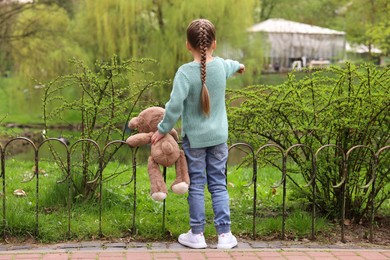 Photo of Little girl with teddy bear outdoors, back view