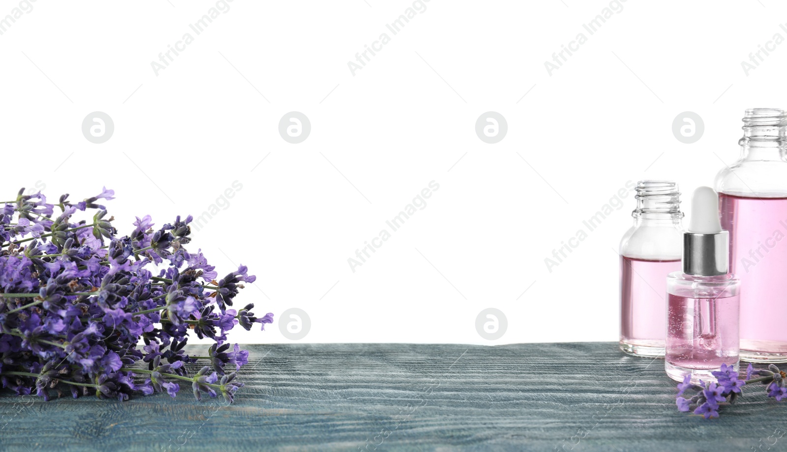 Photo of Bottles of essential oil and lavender flowers on blue wooden table against white background