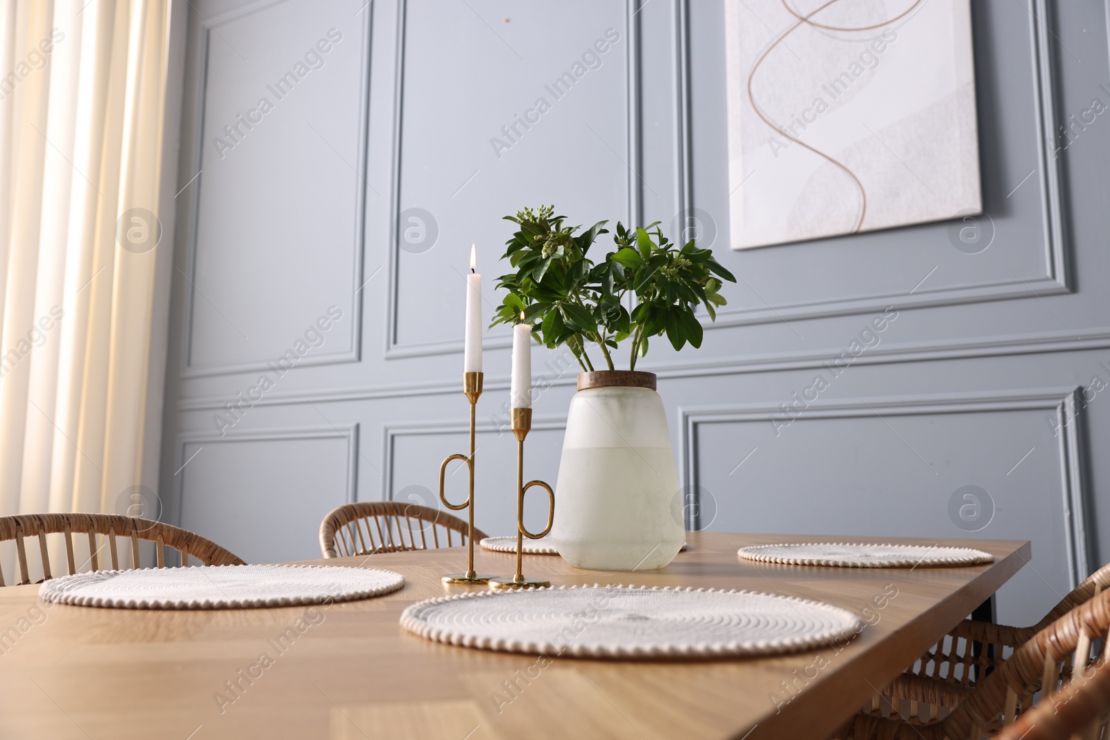 Photo of Vase with green branches and burning candles on wooden table in stylish dining room