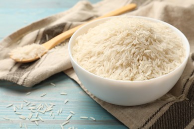 Photo of Raw basmati rice in bowl and spoon on light blue wooden table, closeup. Space for text