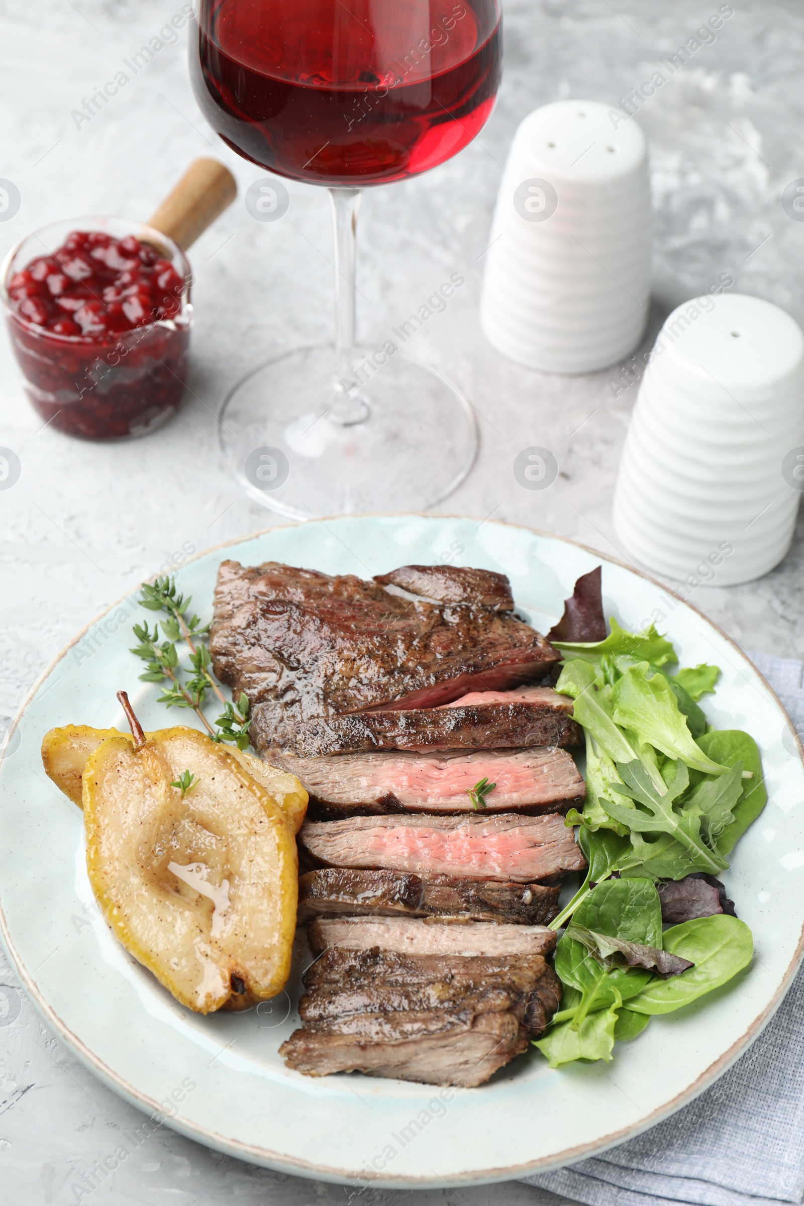 Photo of Delicious roasted beef meat, caramelized pear and greens served on light table