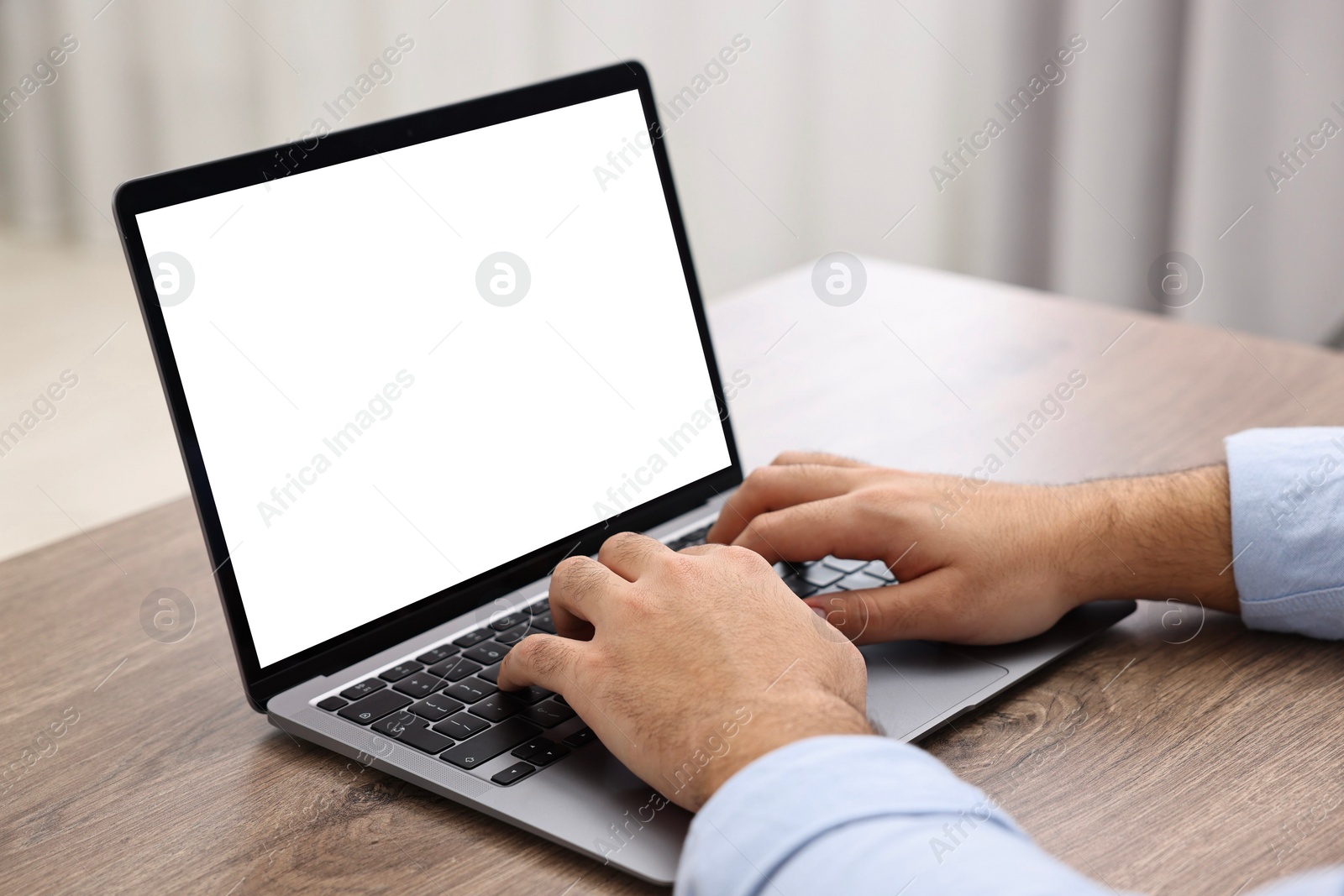 Photo of E-learning. Young man using laptop at wooden table indoors, closeup