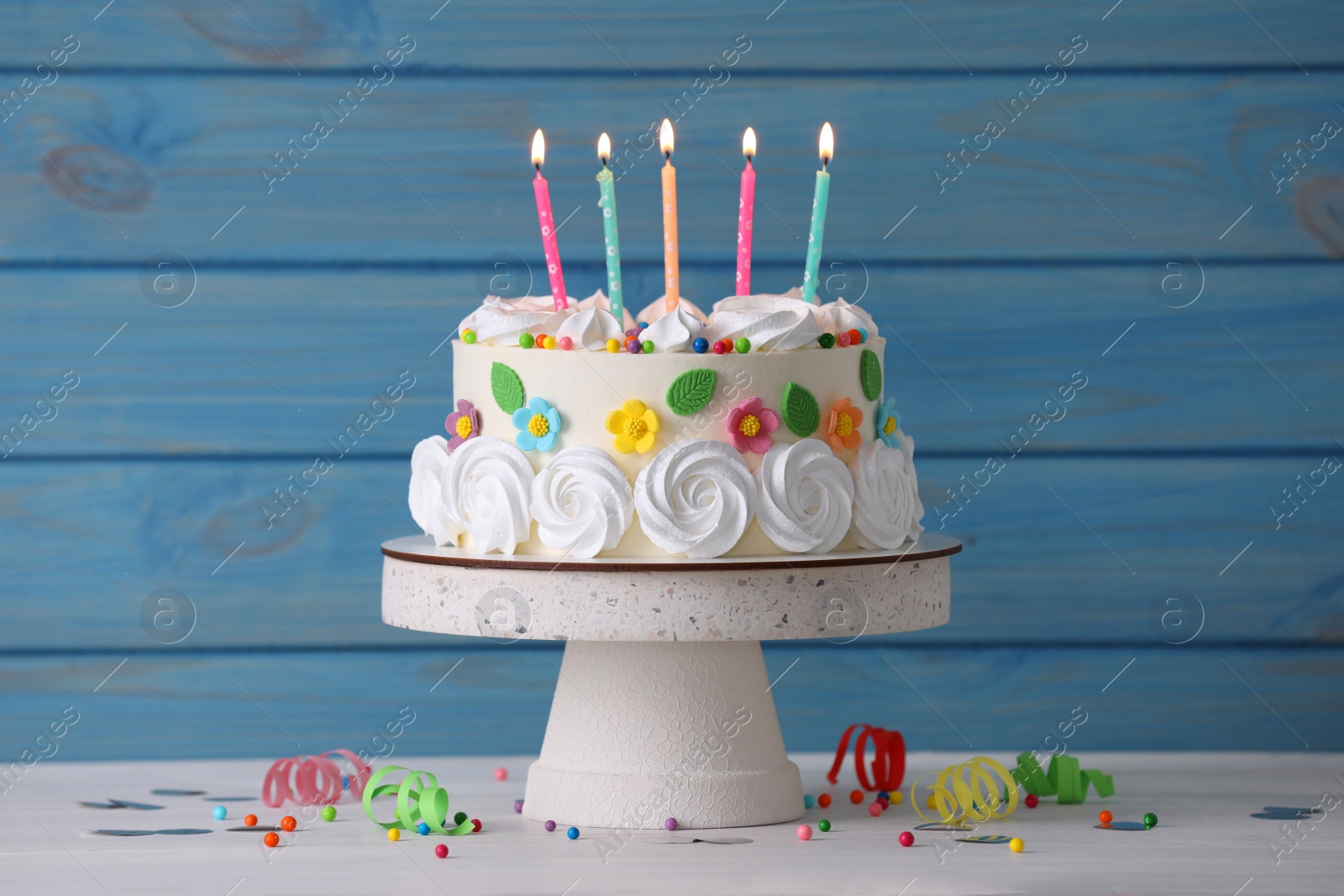 Photo of Delicious birthday cake and party decor on white wooden table against light blue background