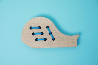 Photo of Wooden whale figure with holes and lace on light blue background, top view. Educational toy for motor skills development