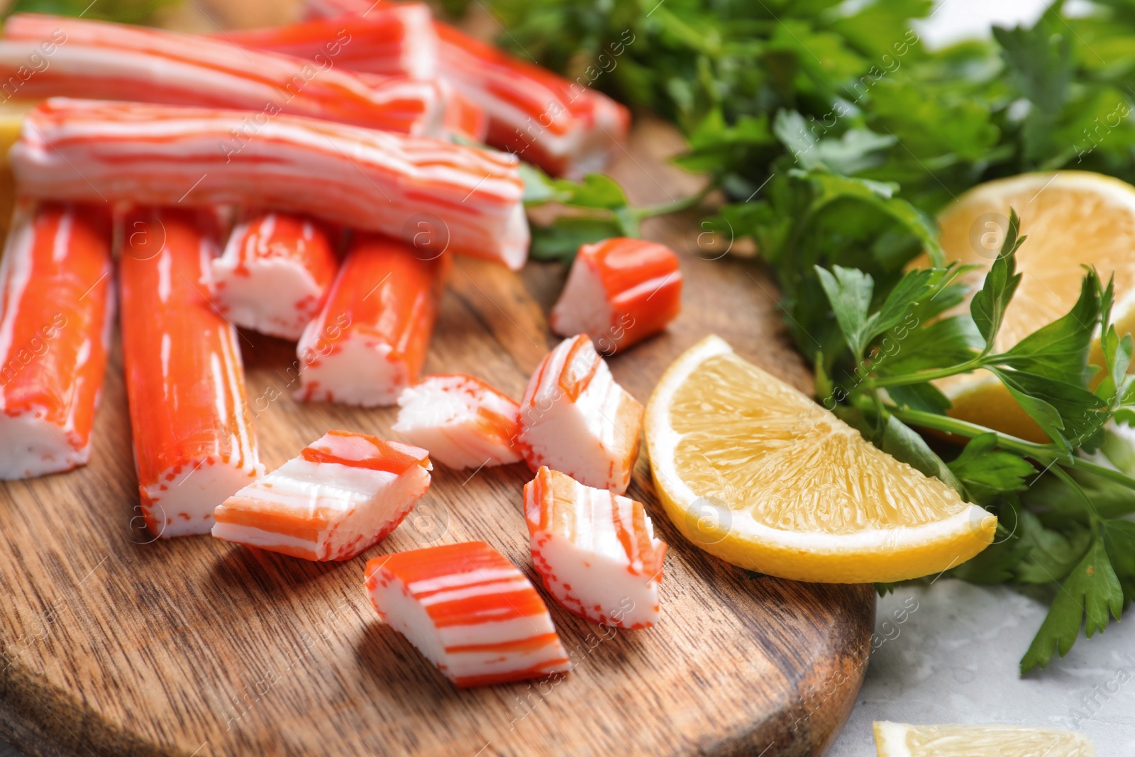 Photo of Delicious crab sticks with lemon and parsley on wooden board, closeup