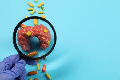 Photo of Endocrinologist looking at model of thyroid gland and capsules through magnifying glass on light blue background, closeup. Space for text