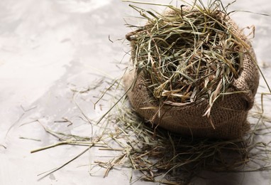 Dried hay in burlap sack on light grey textured table, above view. Space for text