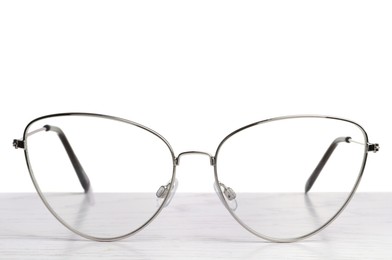 Photo of Stylish glasses with metal frame on wooden table against white background