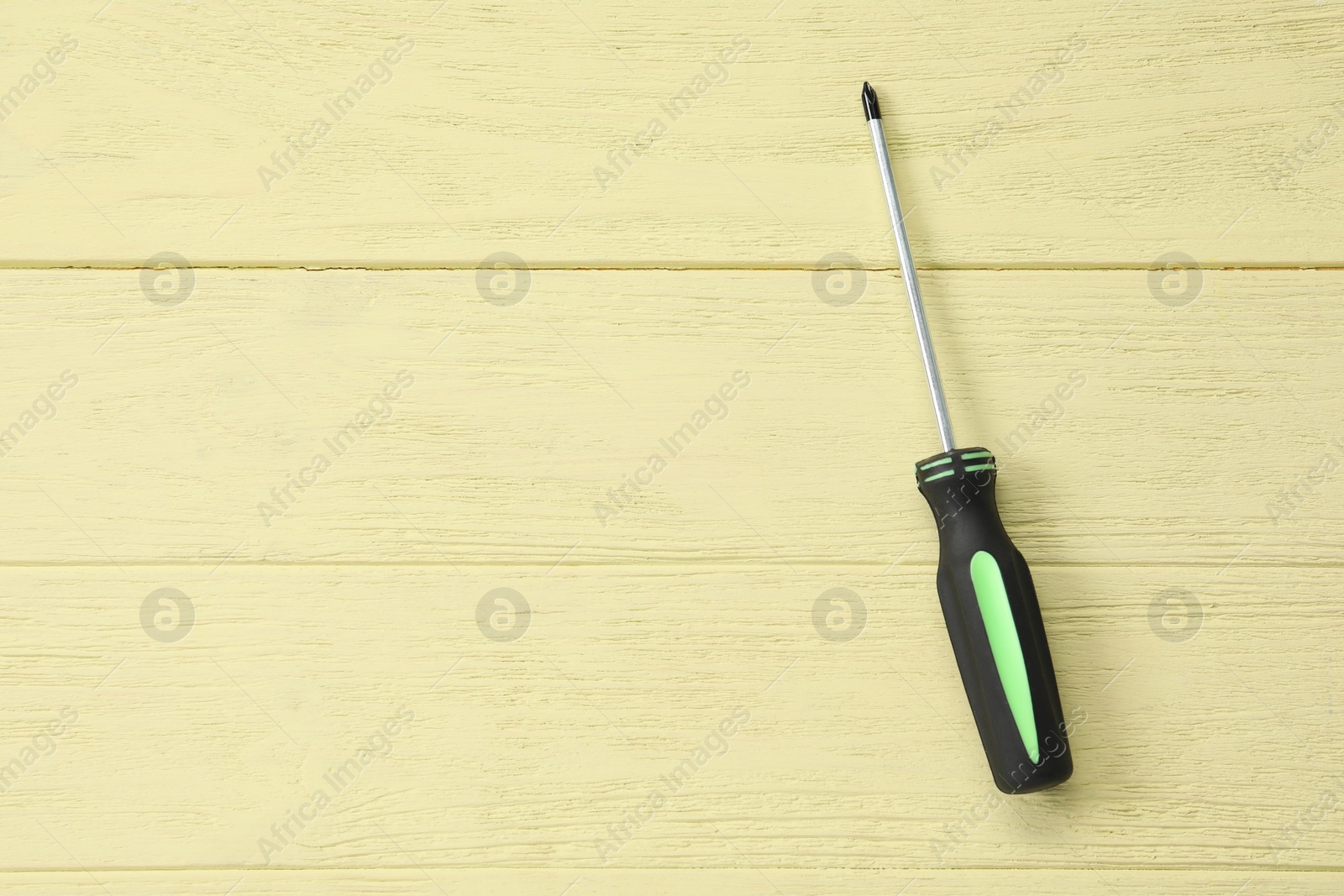 Photo of Screwdriver with black handle on yellow wooden table, top view. Space for text