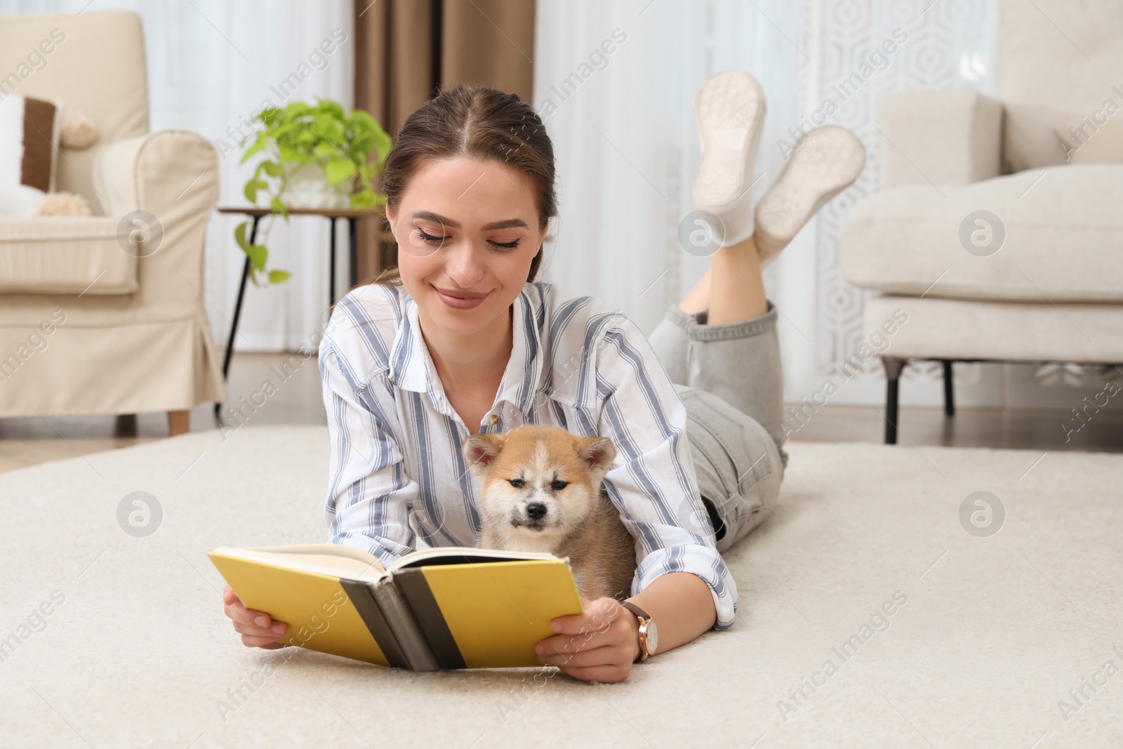 Photo of Happy young woman reading book with cute dog on floor in living room