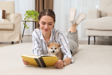 Photo of Happy young woman reading book with cute dog on floor in living room