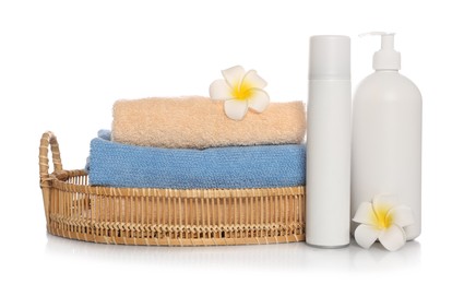 Soft towels in wicker basket, bottles of cosmetic products and plumeria flowers on white background