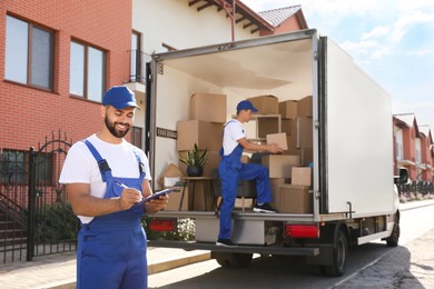 Photo of Moving service workers outdoors, unloading boxes and checking list