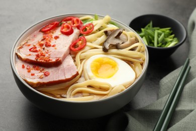 Photo of Delicious ramen in bowl and chopsticks on grey table. Noodle soup