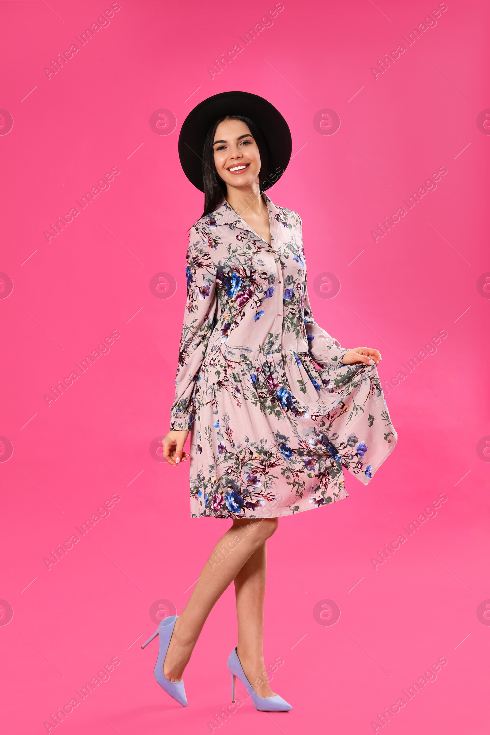 Photo of Young woman wearing floral print dress and stylish hat on pink background