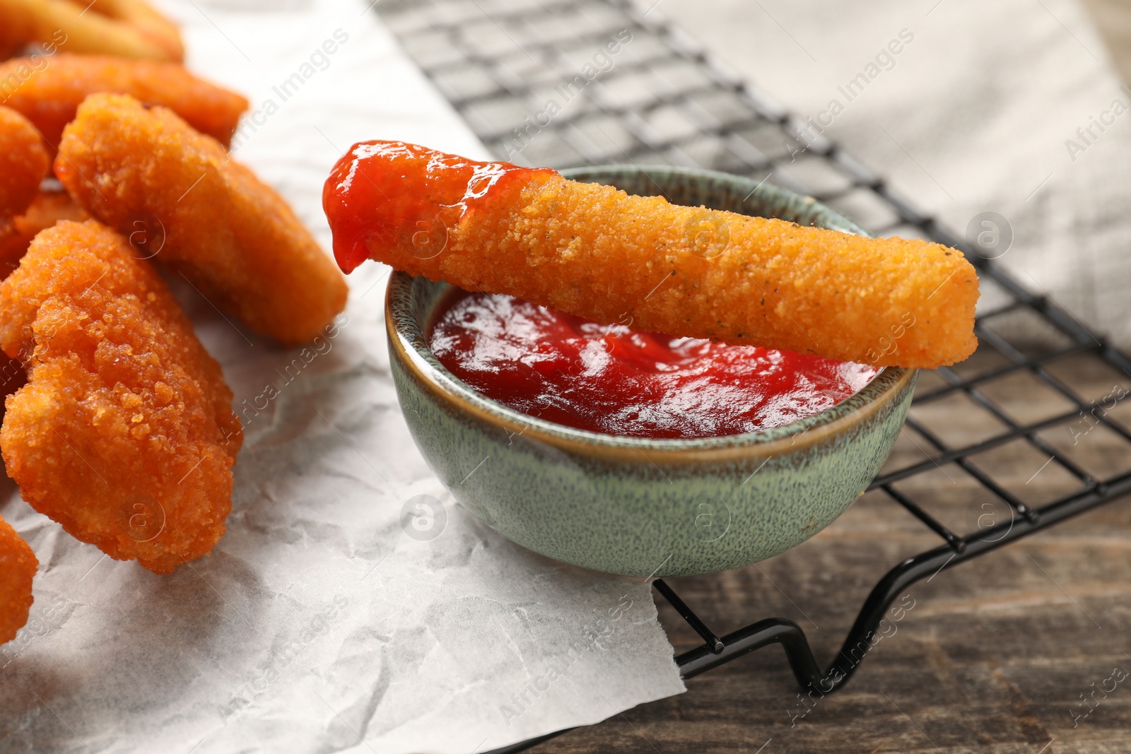 Photo of Tasty chicken nuggets, cheese stick and ketchup on wooden table, closeup