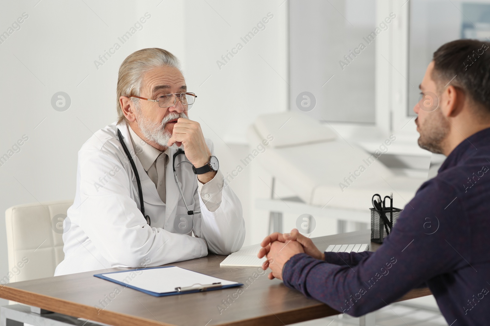 Photo of Senior doctor consulting patient at wooden table in clinic