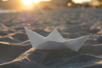 Photo of Beautiful white paper boat on sand outdoors, closeup