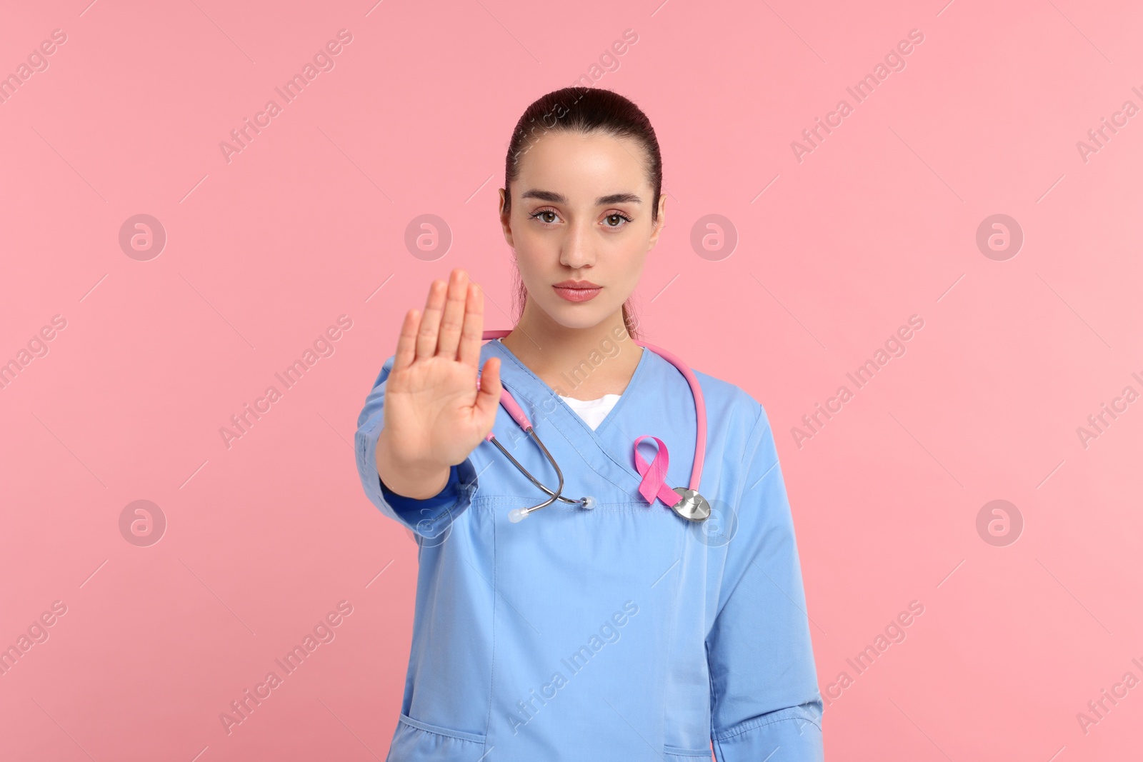 Photo of Mammologist with pink ribbon showing stop gesture on color background. Breast cancer awareness