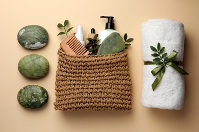 Photo of Compact toiletry bag with different cosmetic products, spa stones and towel on beige background, flat lay